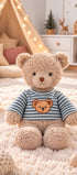  Peluche ours beige Colin de Bukowski Design assise sur un tapis, avec un haut rayé bleu-vert et blanc orné d’une tête d’ours.
