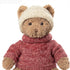 Gros plan de la peluche ours Steve de Bukowski Design, avec un bonnet écru et un pull rouge à col roulé.