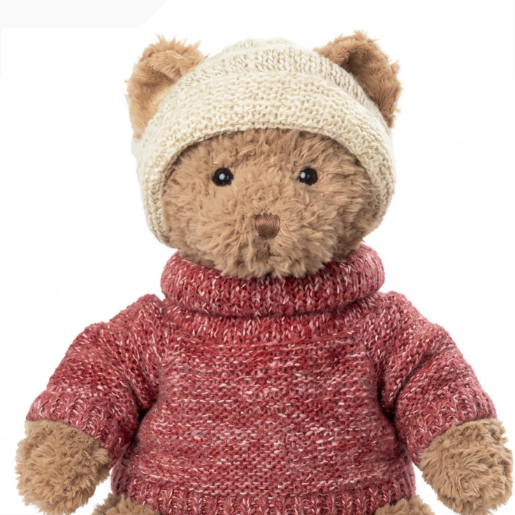 Gros plan de la peluche ours Steve de Bukowski Design, avec un bonnet écru et un pull rouge à col roulé.