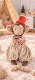 Peluche singe Winston de Bukowski Design assise sur un tapis, les bras croisés, avec un pantalon beige et un chapeau rouge.