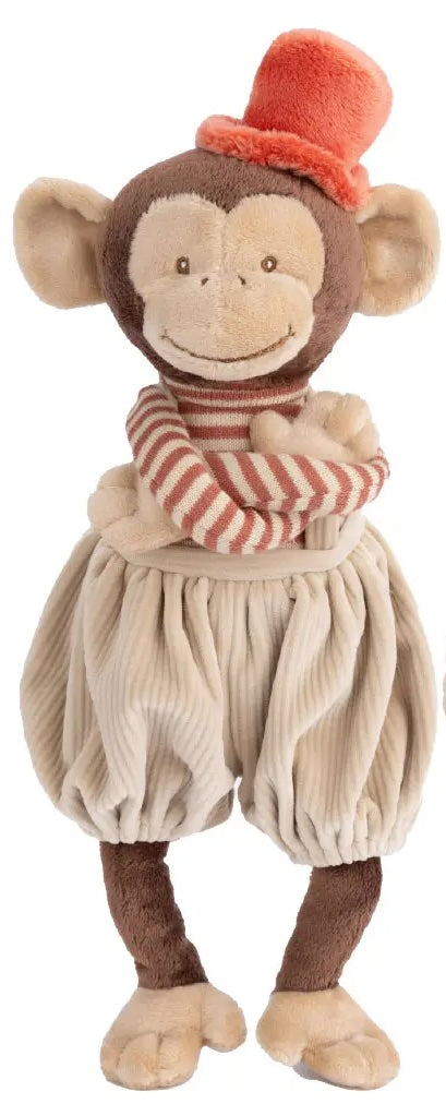 Peluche singe Winston de Bukowski Design sur fond blanc, les bras croisés, avec un pantalon beige, un haut rayé et un chapeau rouge