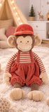 Peluche singe Winston de Bukowski Design assise sur un tapis, en salopette rouge, haut rayé et chapeau rouge