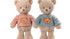  Deux peluches ours Colin de Bukowski Design côte à côte, l’une en haut rayé rouge et blanc, l’autre en haut rayé bleu-vert et blanc.